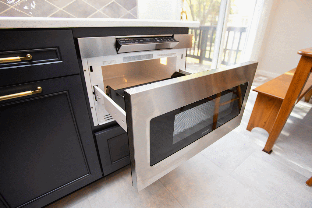 A built-in microwave drawer with a stainless steel finish is open in a modern kitchen.