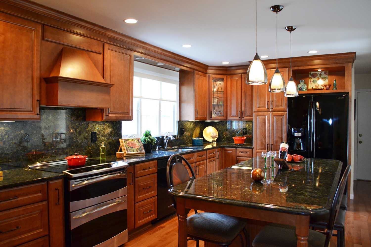 Modern kitchen with wood cabinets, black granite countertops, island with seating, stainless steel appliances, pendant lights, and a black refrigerator.