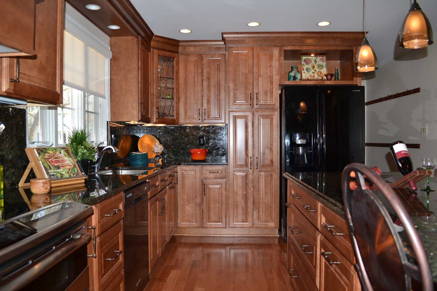 Modern kitchen with wooden cabinets, black appliances, granite countertops, pendant lights, and various kitchen items on the counters.