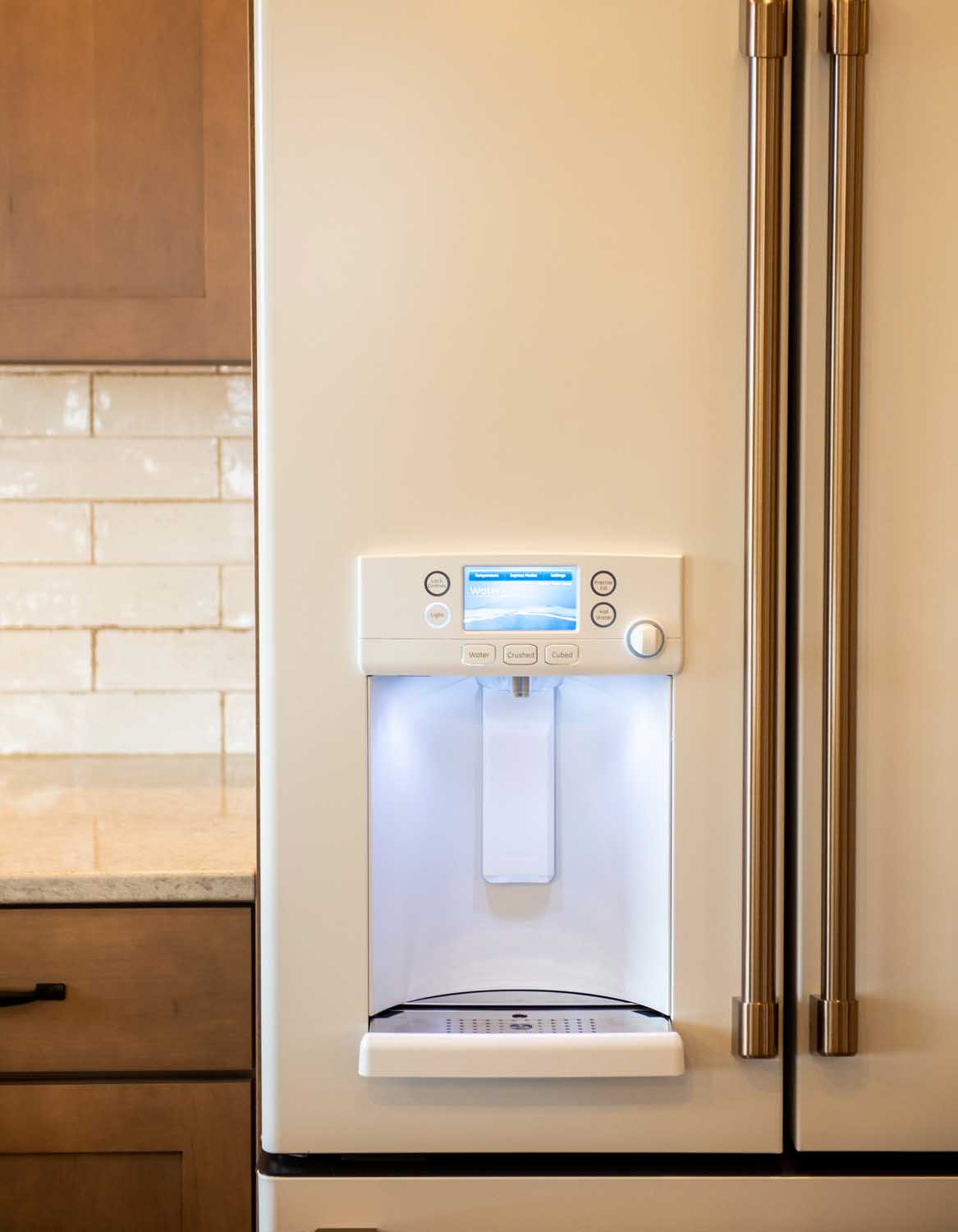 A close-up of a refrigerator door with a built-in water and ice dispenser, illuminated and displaying a digital screen.