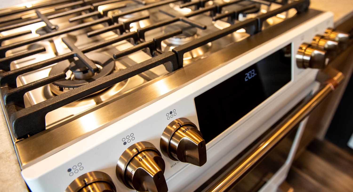 Close-up of a stainless steel gas stove with four burners, control knobs, and a digital display panel on the front.