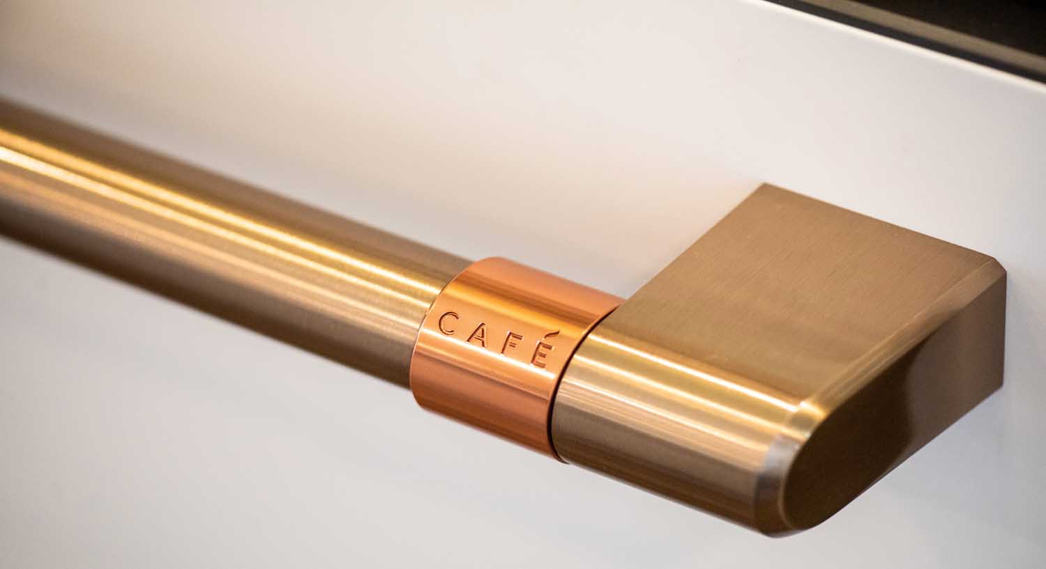 Close-up of a metallic gold and copper appliance handle with the word "CAFÉ" engraved on a copper accent.