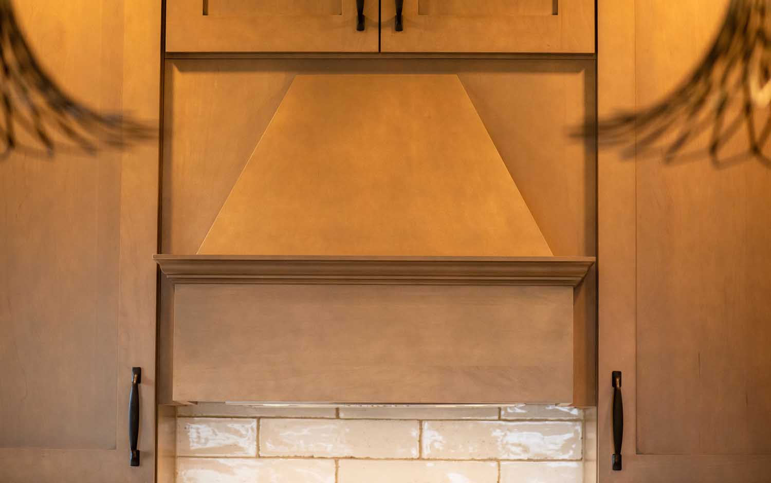 Close-up of a wooden kitchen cabinet with a geometric design above a tiled backsplash, featuring metal handles on adjacent cabinet doors.