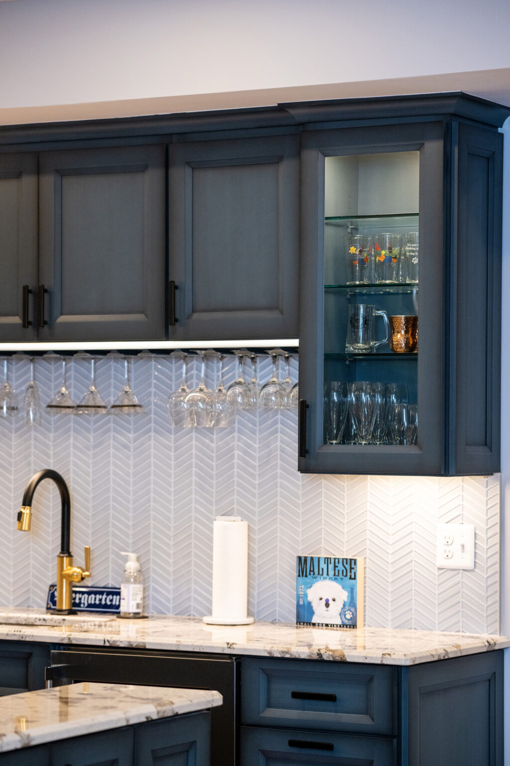 Glass front cabinetry showcases some stemware and other novelty bar glasses in this finished basement.