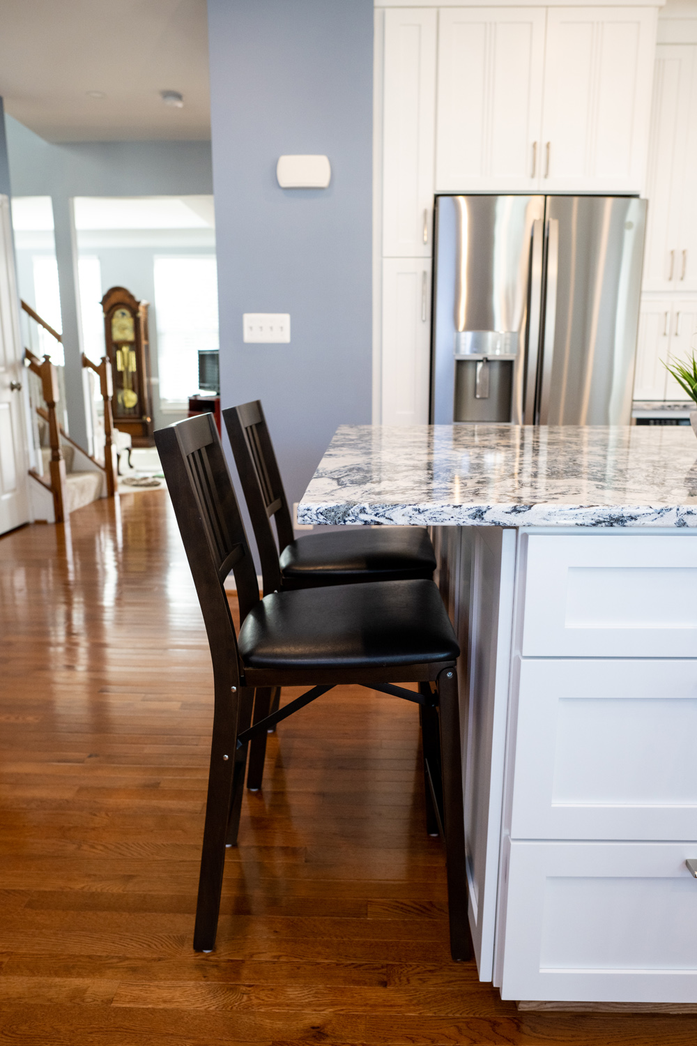 Three black chairs are lined up at a kitchen island with a blue and white countertop in a room with wooden floors and white cabinets.