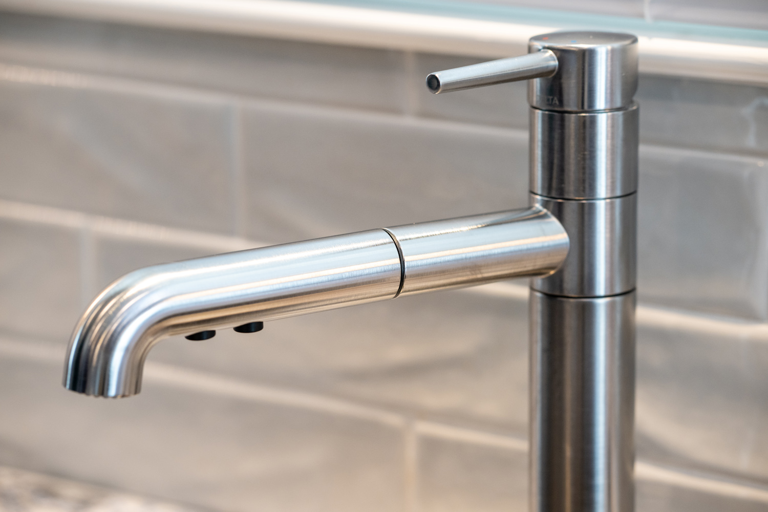 Close-up of a modern stainless steel kitchen faucet with a lever handle, set against a tiled backsplash.