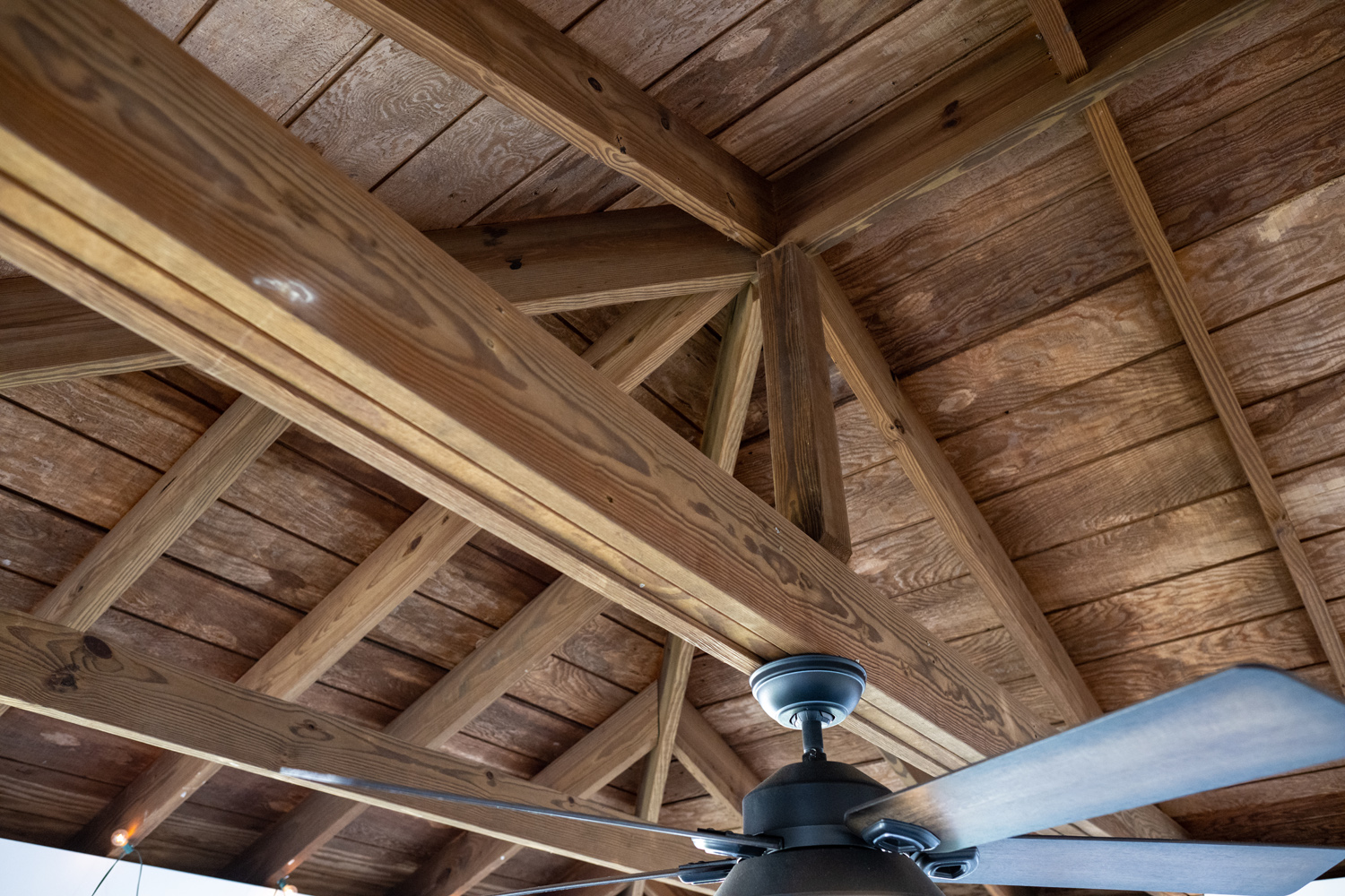 Exposed wooden beams and planks form a pitched ceiling, with a ceiling fan and light fixture attached below.
