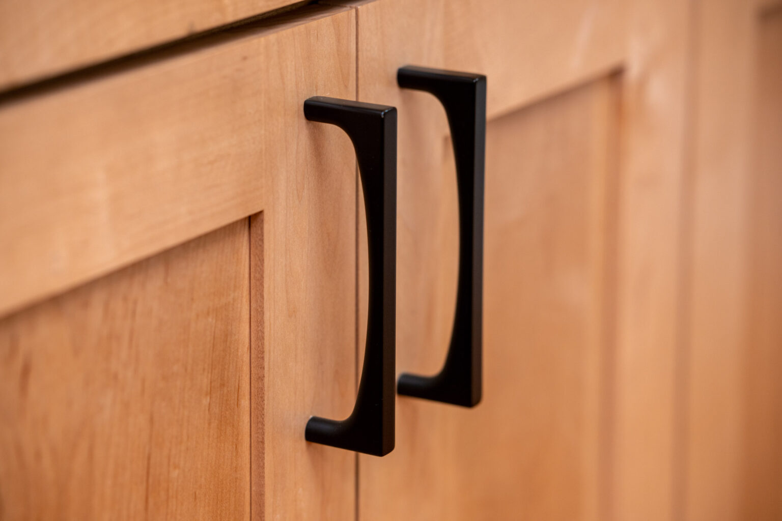 Close-up of two black metal handles on light wood cabinet doors.