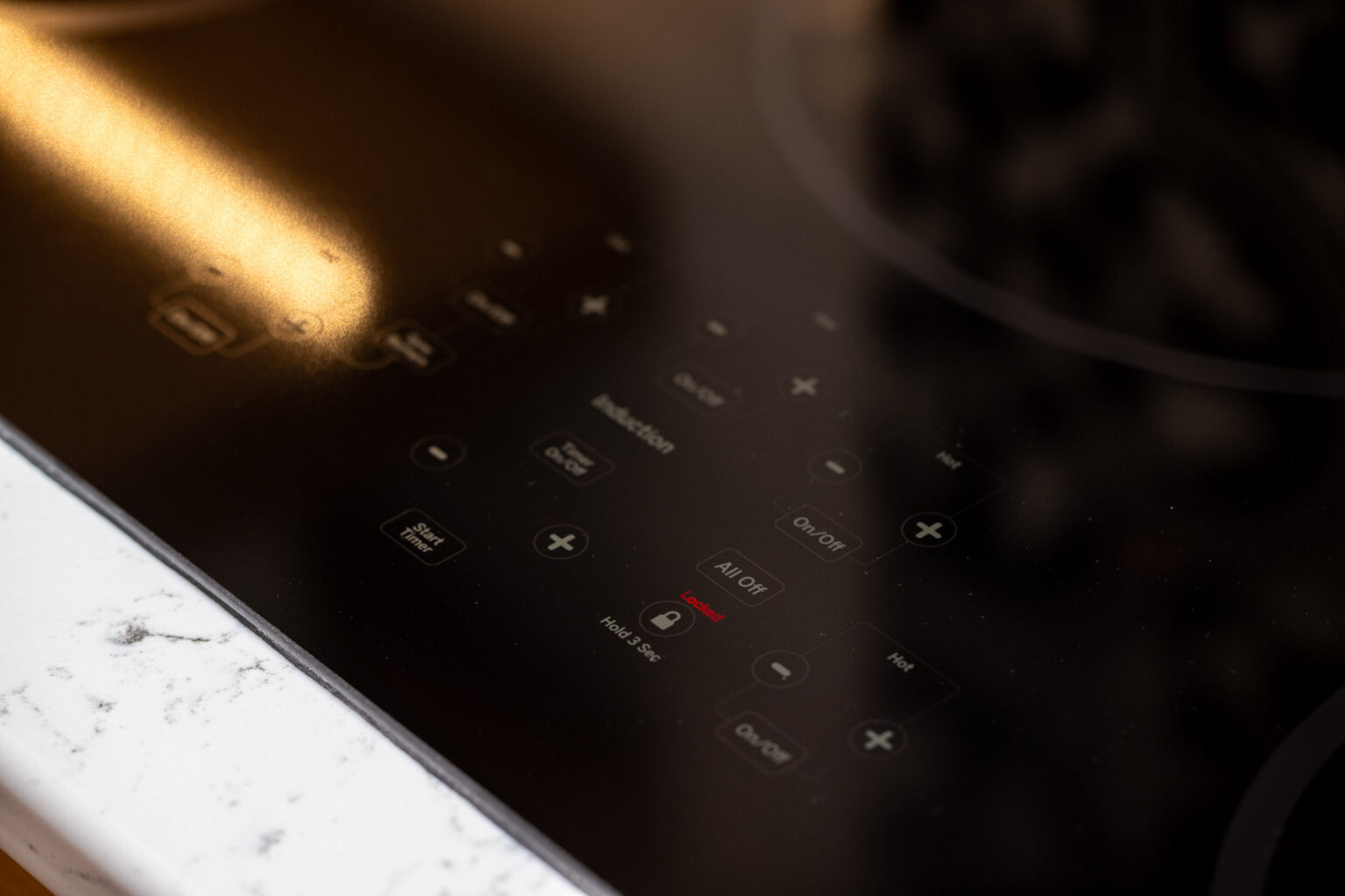 Close-up of a black glass induction cooktop with touch controls and digital display on a white countertop.