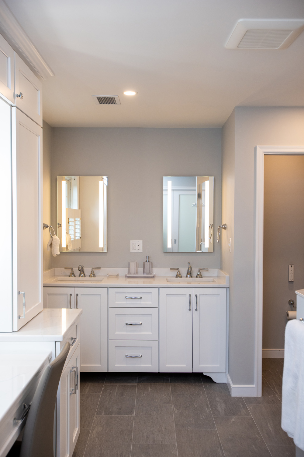 Modern bathroom with double sinks, two mirrors, white cabinets, gray tiled floor, and neutral wall colors.
