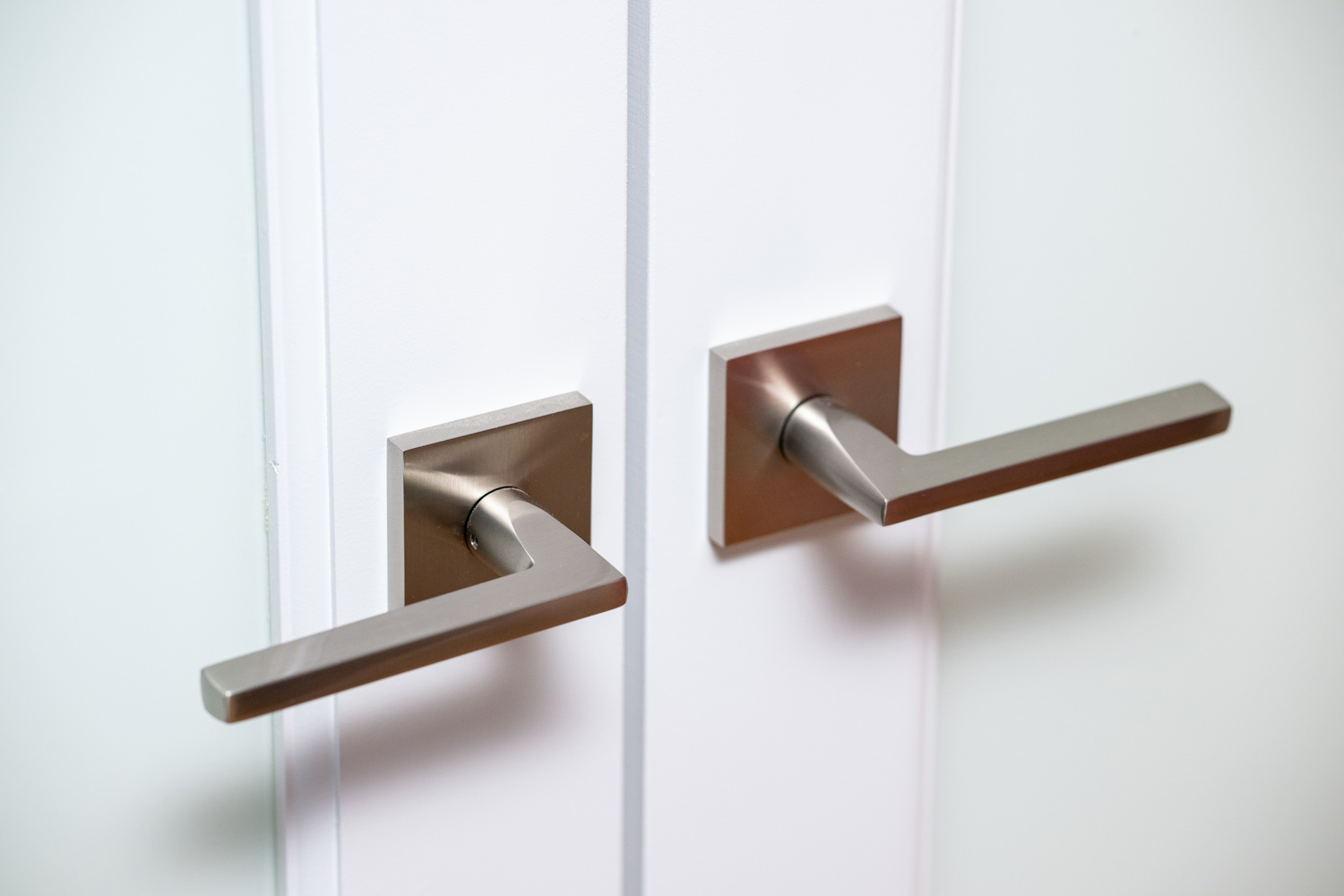 Two modern silver door handles on a white double door, positioned symmetrically and facing opposite directions.