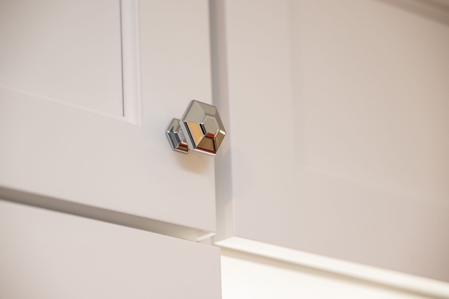 Close-up of a metallic, hexagonal cabinet knob mounted on a white cabinet door with simple panel detailing.