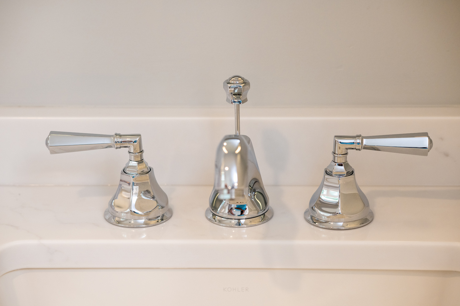 Close-up of a modern chrome bathroom sink faucet with two handles and a central spout, mounted on a white countertop.