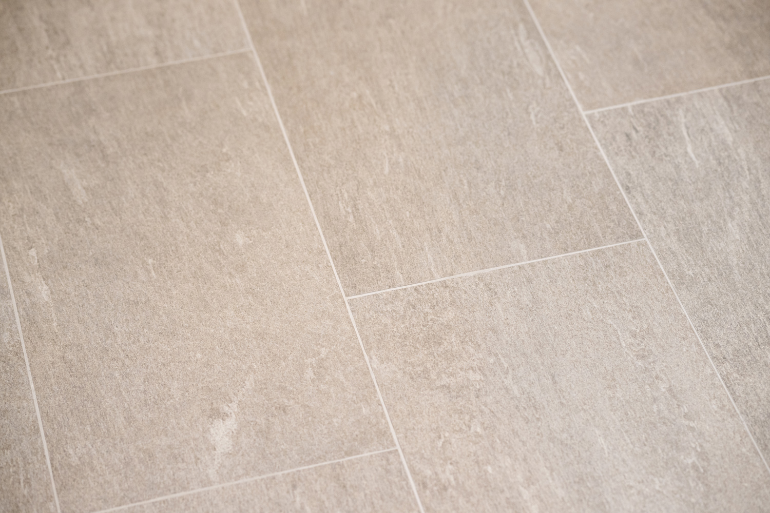 Close-up of beige rectangular ceramic tiles with light grout lines, arranged in a staggered pattern on a floor.