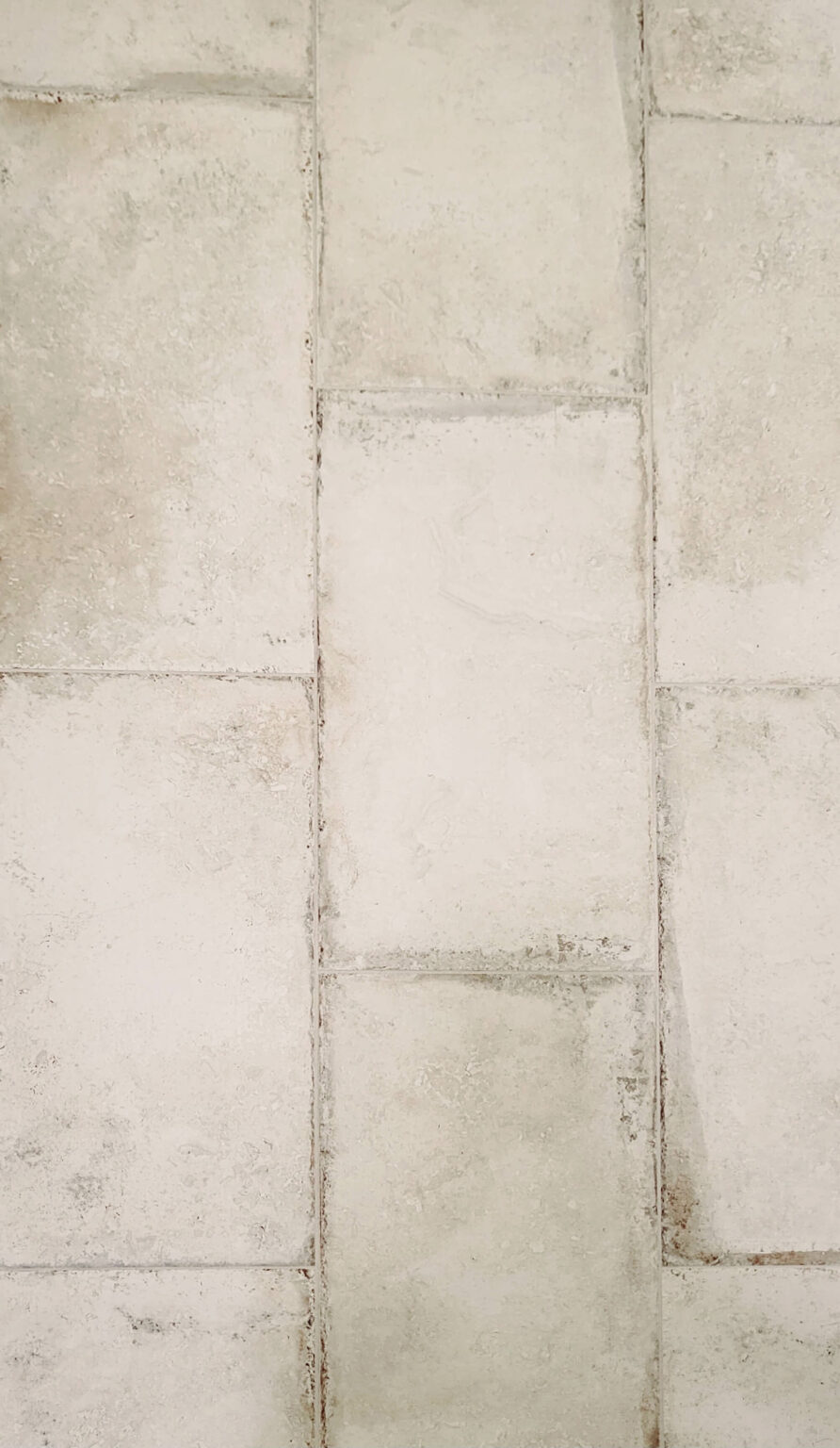 Close-up view of a textured surface with rectangular, off-white tiles and visible grout lines.