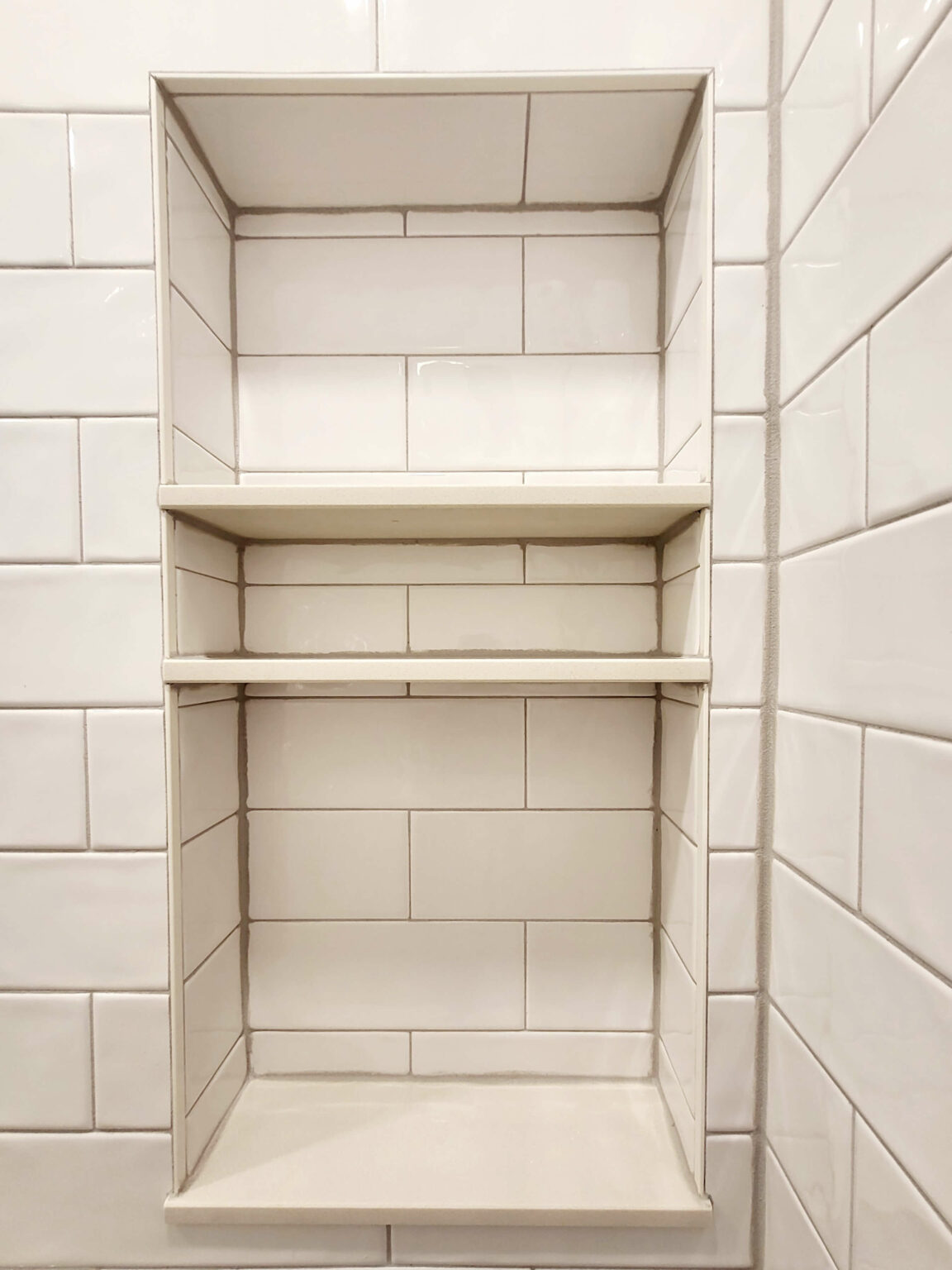 Built-in shower niche with three empty shelves, surrounded by white rectangular tiles arranged in a staggered pattern.