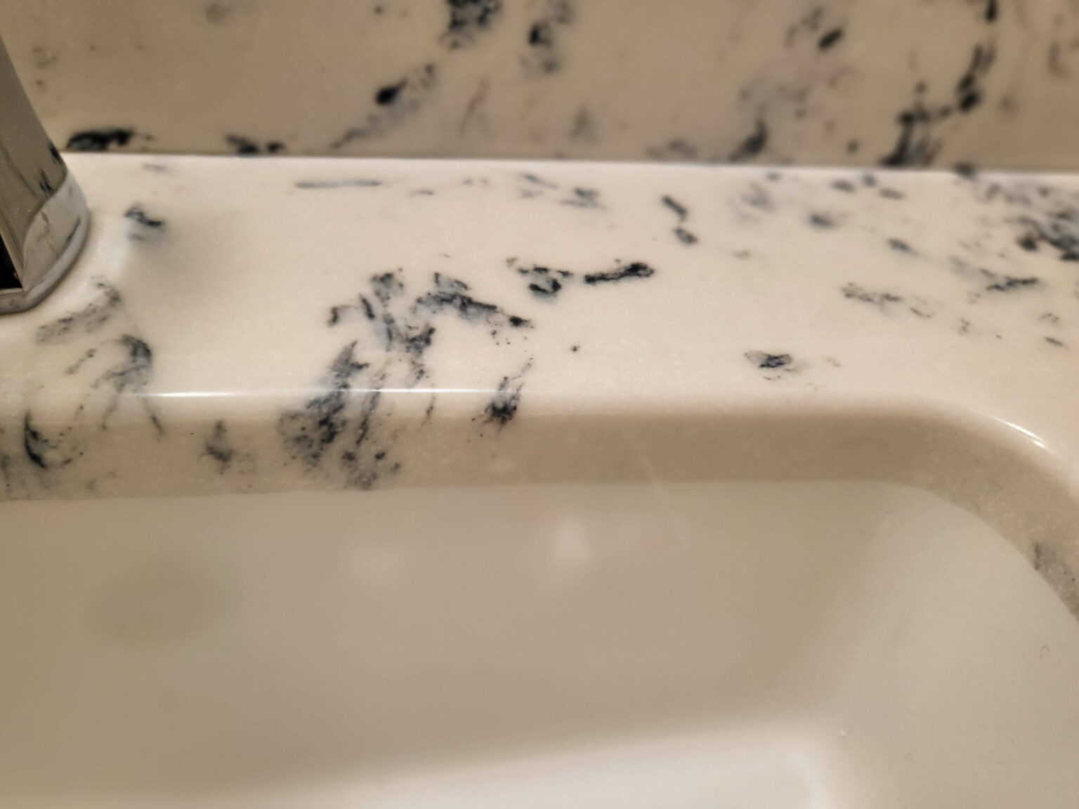 Close-up of a white marble bathroom sink countertop with dark gray and black veining patterns.