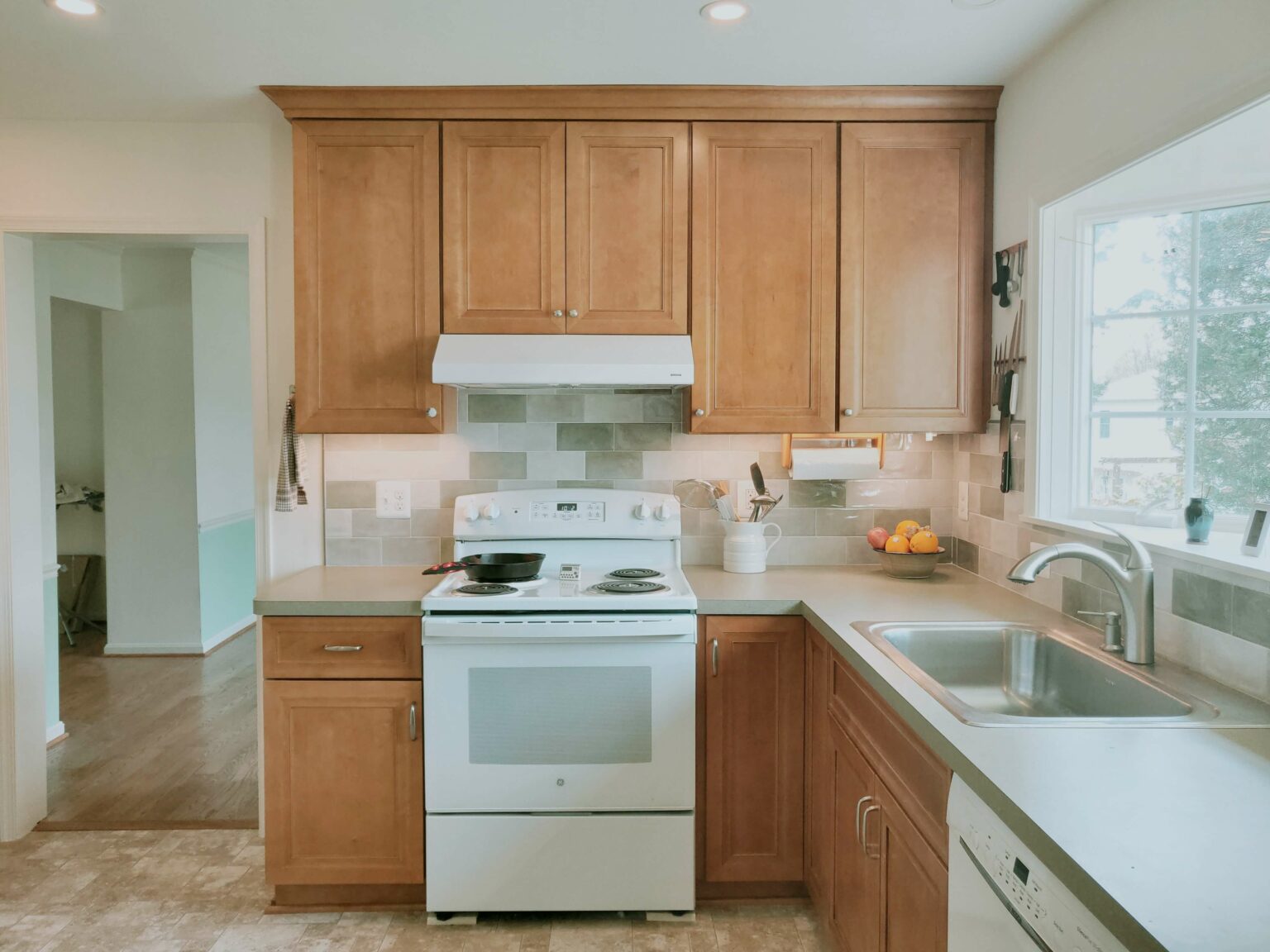 A kitchen with wooden cabinets, white appliances, a stove with a pan, a countertop with utensils, and a window above the sink.