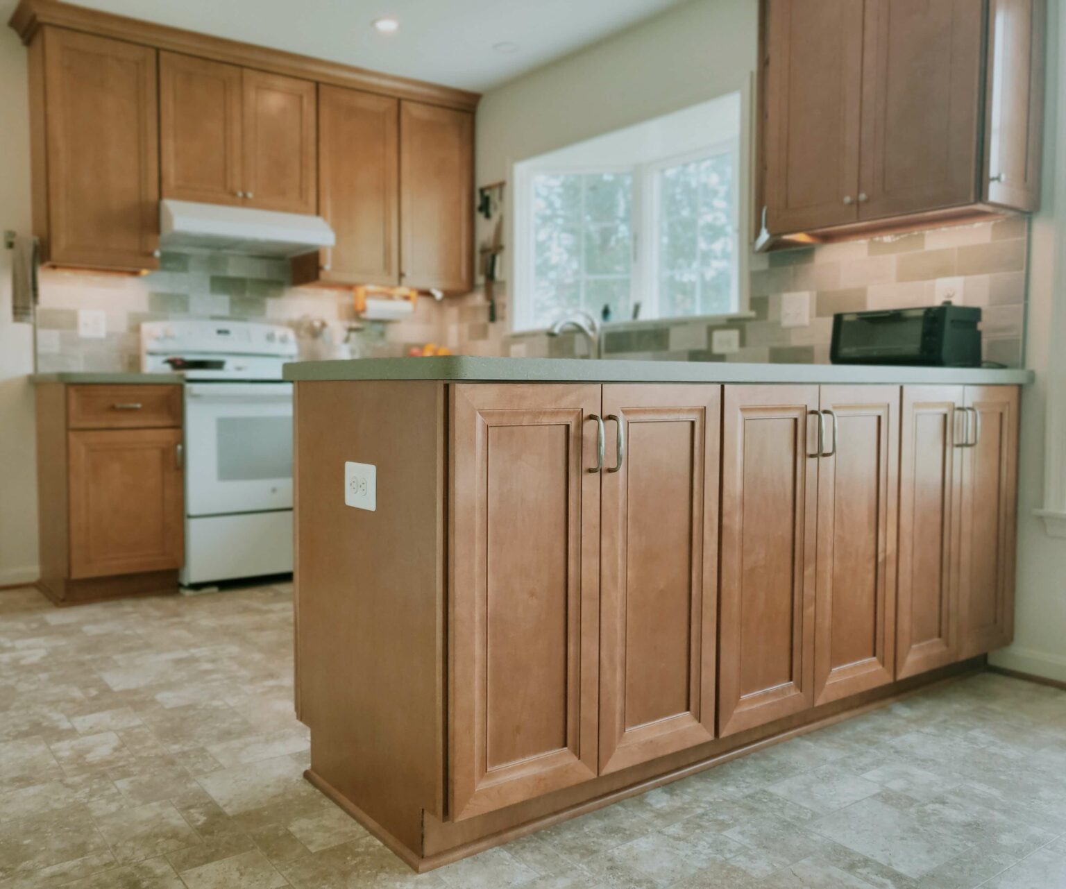 Spacious kitchen with wood cabinets, a center island, white appliances, tiled backsplash, and large window providing natural light.