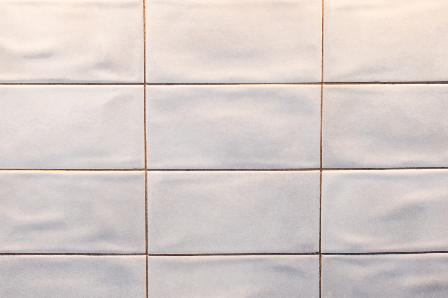 A close-up view of a wall with glossy, rectangular white tiles arranged in a grid pattern.