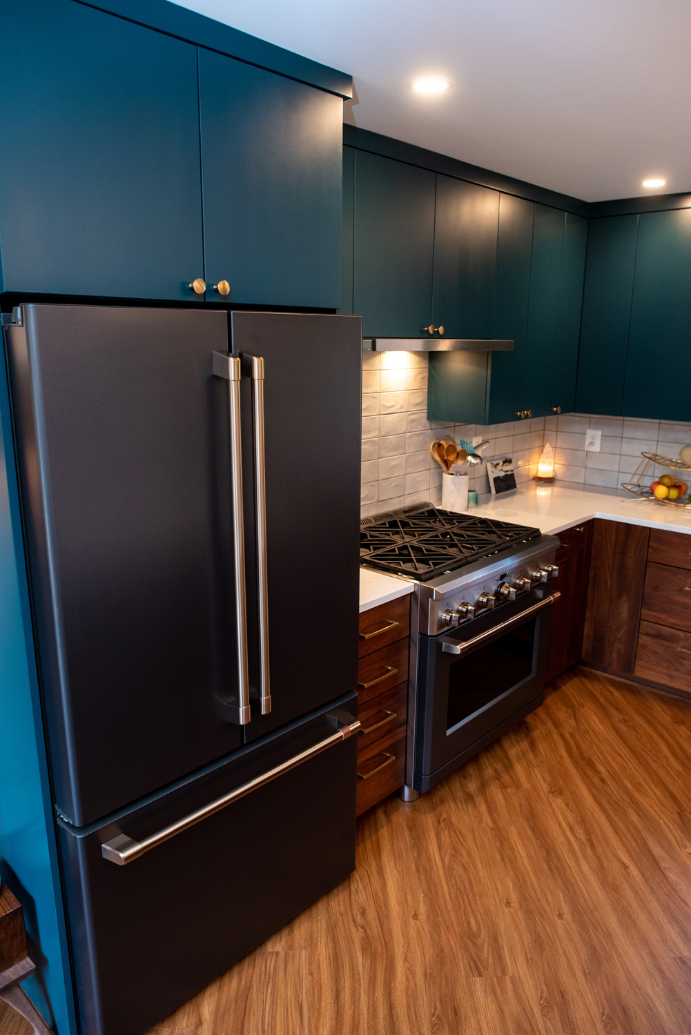 Modern kitchen with dark blue cabinets, stainless steel appliances, a black refrigerator, gas range, white backsplash, and wood flooring.