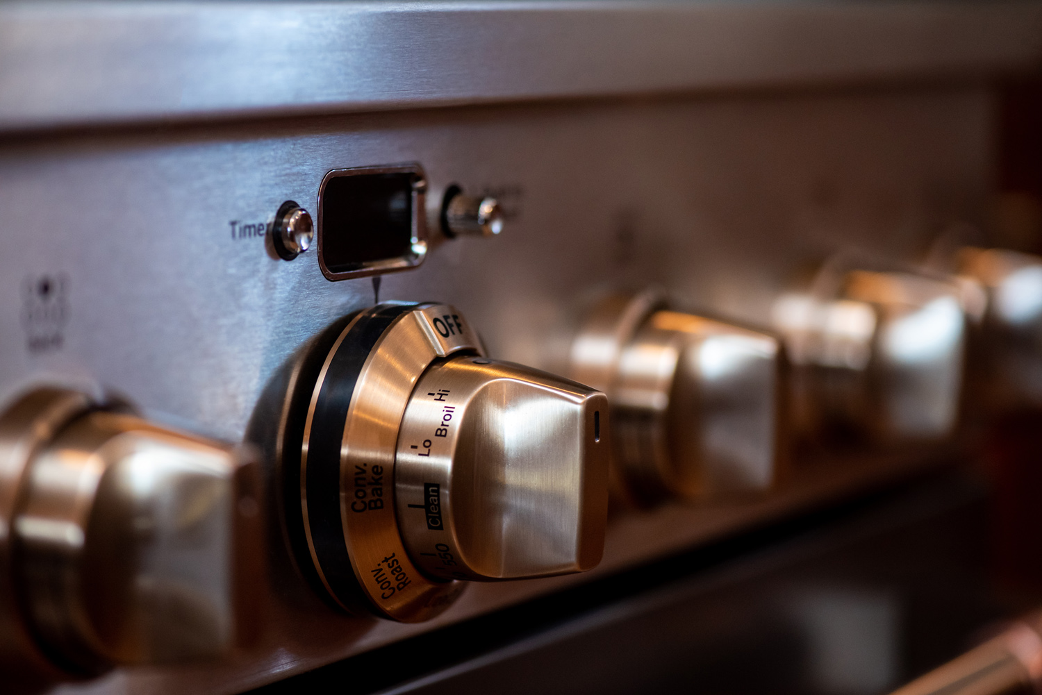 Close-up of stainless steel oven control knobs, with one knob set to "Off" and visible temperature and setting labels.