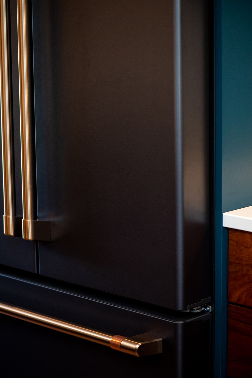 Close-up of a modern black refrigerator with gold handles, next to a wooden cabinet and a white countertop.
