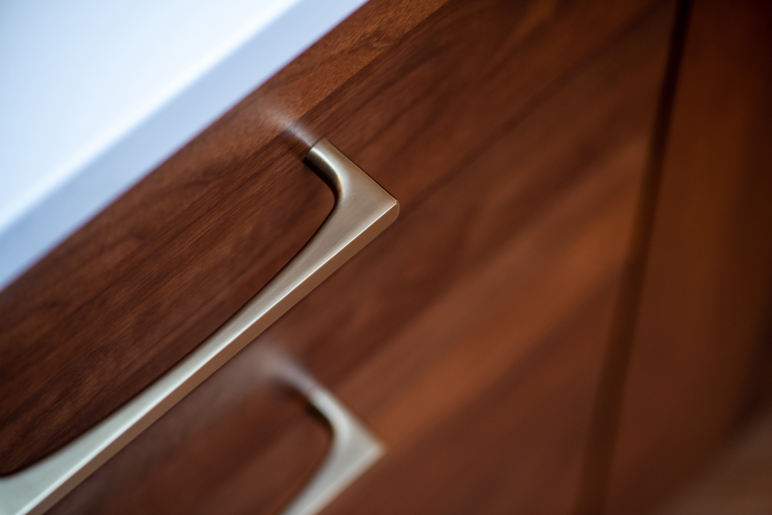 Close-up of two bronze handles on wooden kitchen cabinet doors beneath a white countertop.