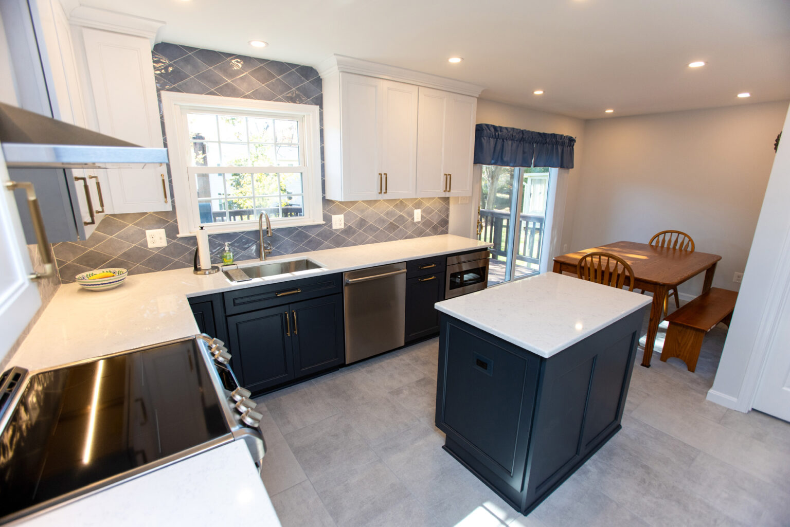 Modern kitchen with dark blue lower cabinets, white upper cabinets, stainless steel appliances, a center island, and a dining area.
