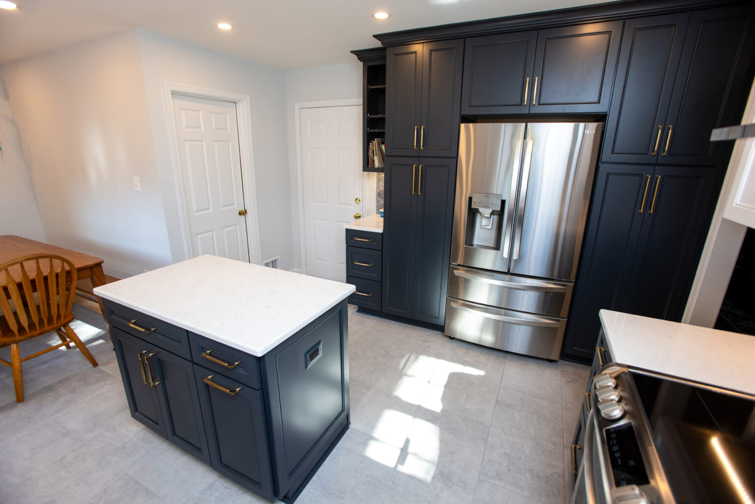 Modern kitchen featuring dark cabinets, stainless steel appliances, and a white countertop island. The space is well-lit with recessed lighting and includes a wooden dining table with chairs.