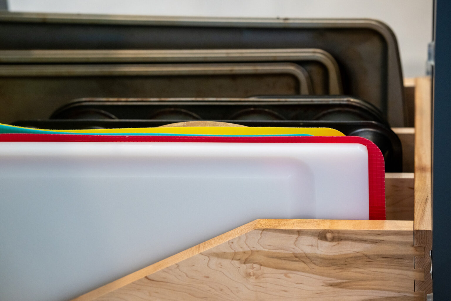 A wooden rack holds several neatly organized cutting boards and baking sheets of different colors and materials.