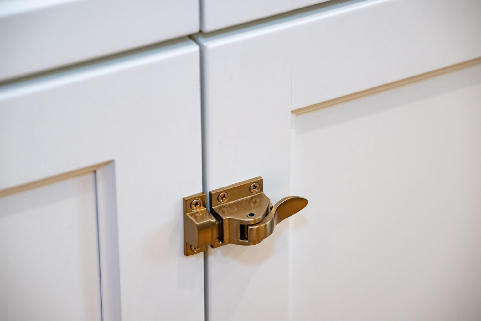 Image by Lesnick Photo A brass latch lock secures the doors of a white cabinet.