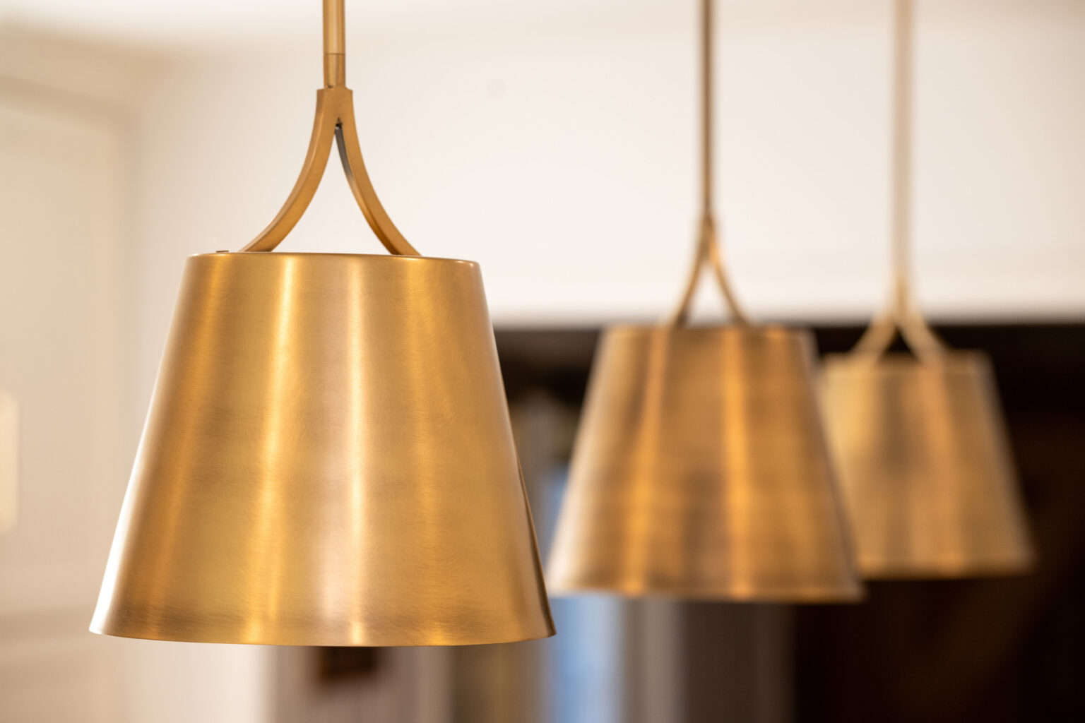 Image by Lesnick Photo Three close-up views of golden pendant lights hanging from the ceiling with a blurred background.