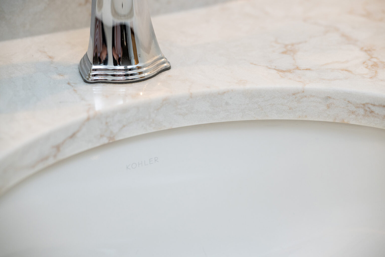 Close-up of a bathroom sink with a marble countertop and a chrome faucet. The sink is labeled with the brand "Kohler.