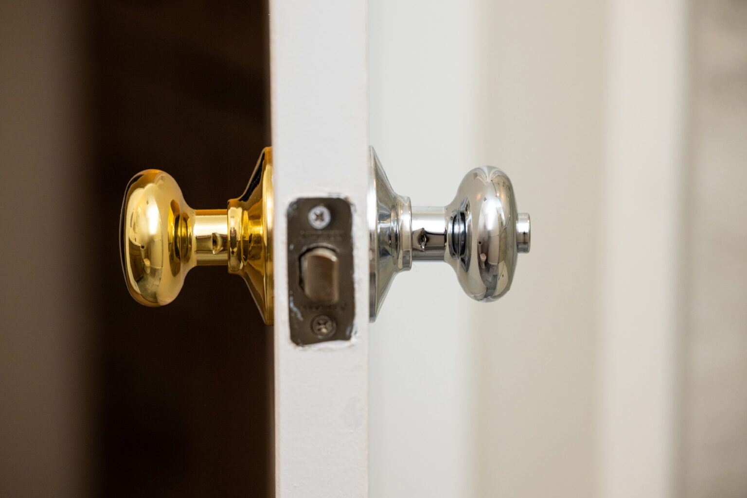 A door with one gold and one silver doorknob is slightly ajar, revealing a latch mechanism in the middle.