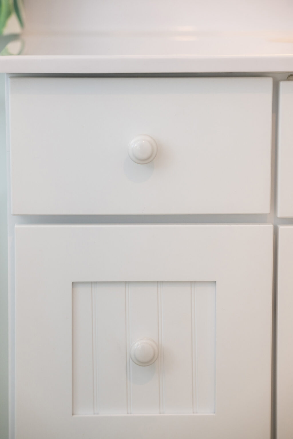 Image by Lesnick Photo Close-up of a white cabinet with two drawers, each featuring a round, white knob. The lower drawer has a vertical line pattern.