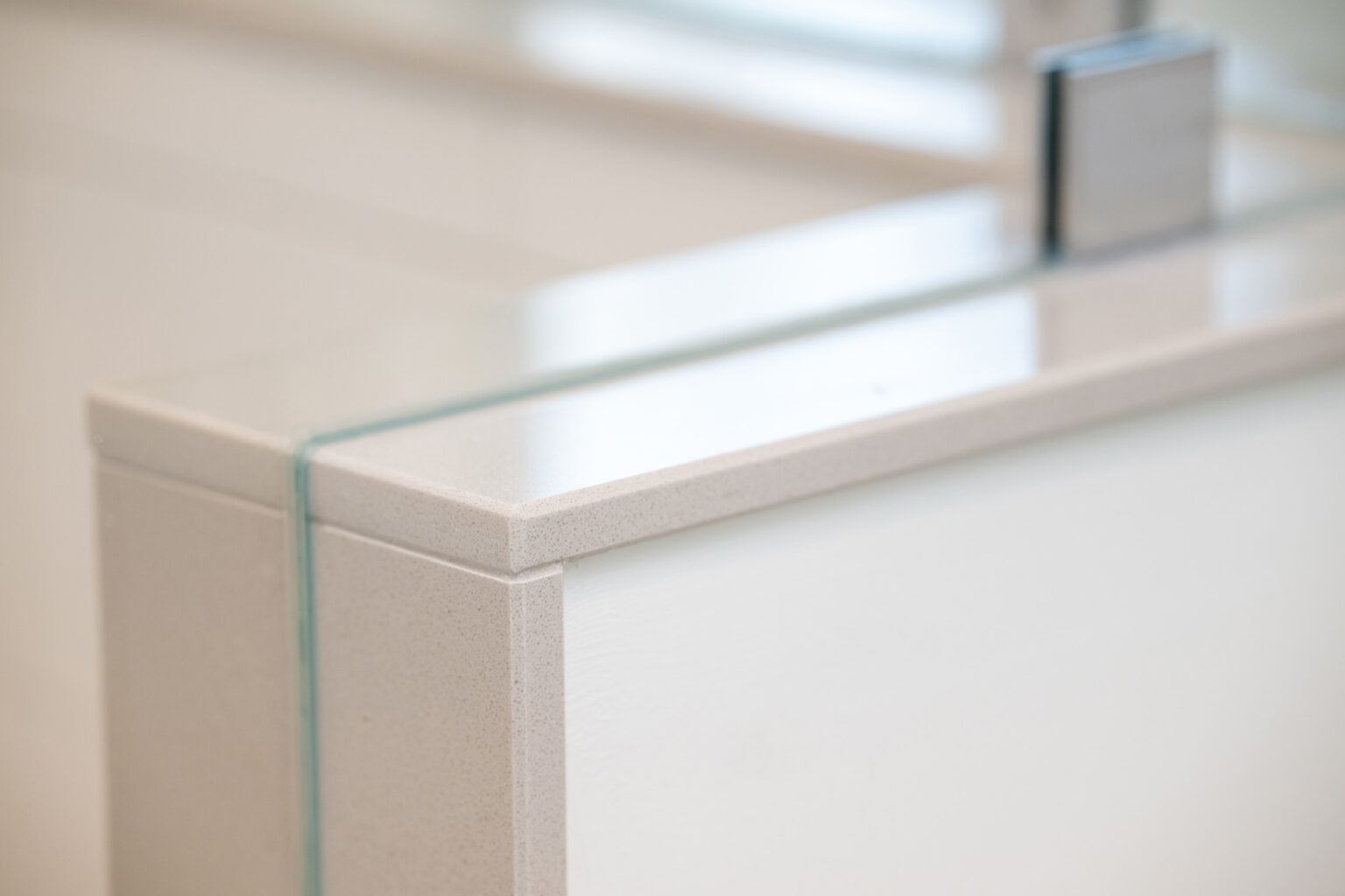 Image by Lesnick Photo Close-up of a modern bathroom counter edge with a squared-off design, featuring a smooth, light-colored surface and a clear section of glass running vertically.