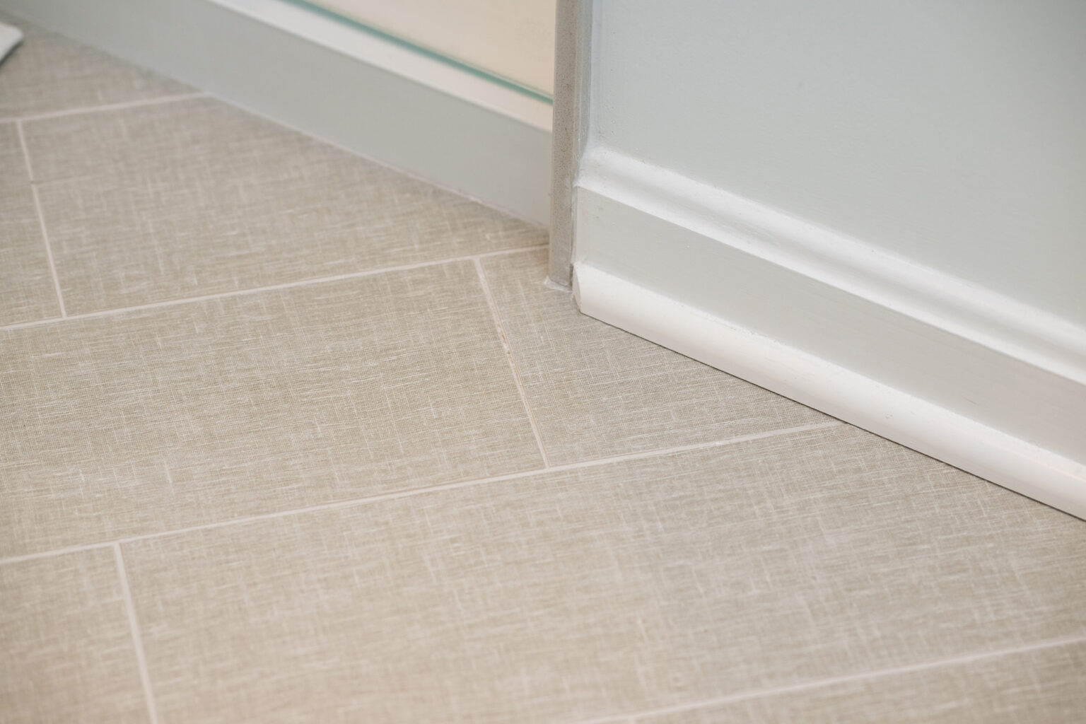 Image by Lesnick Photo Close-up of a corner of a room with beige tiled flooring, a white baseboard, and light gray painted walls.