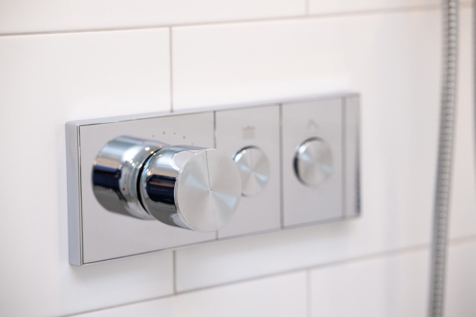 Image by Lesnick Photo Close-up of a modern shower control panel with three round metal knobs mounted on a white tiled wall.