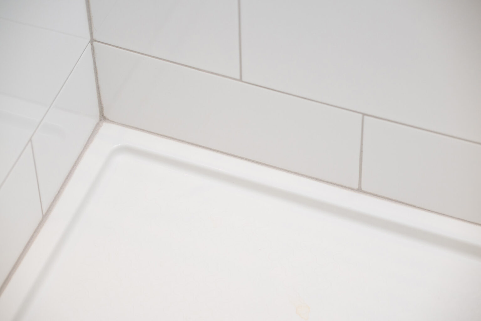 Image by Lesnick Photo A tiled shower corner with white grout and clean white tiles, showing a smooth transition between the tile and the shower tray.