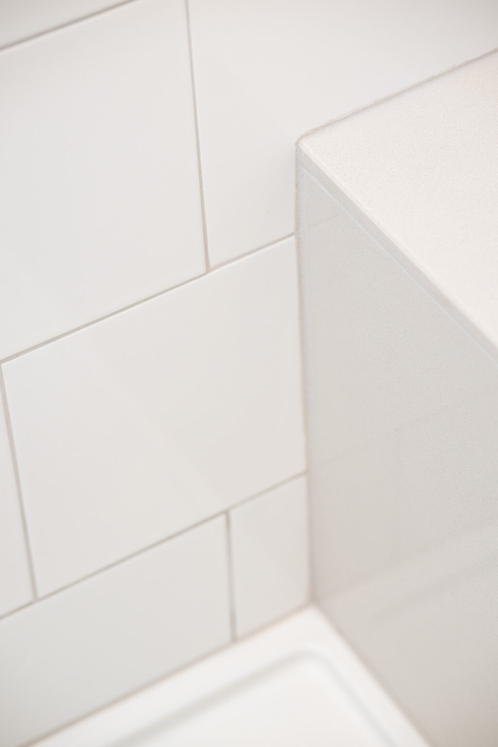Image by Lesnick Photo A close-up of a white tiled wall with a corner edge, featuring large rectangular tiles and a white countertop surface.