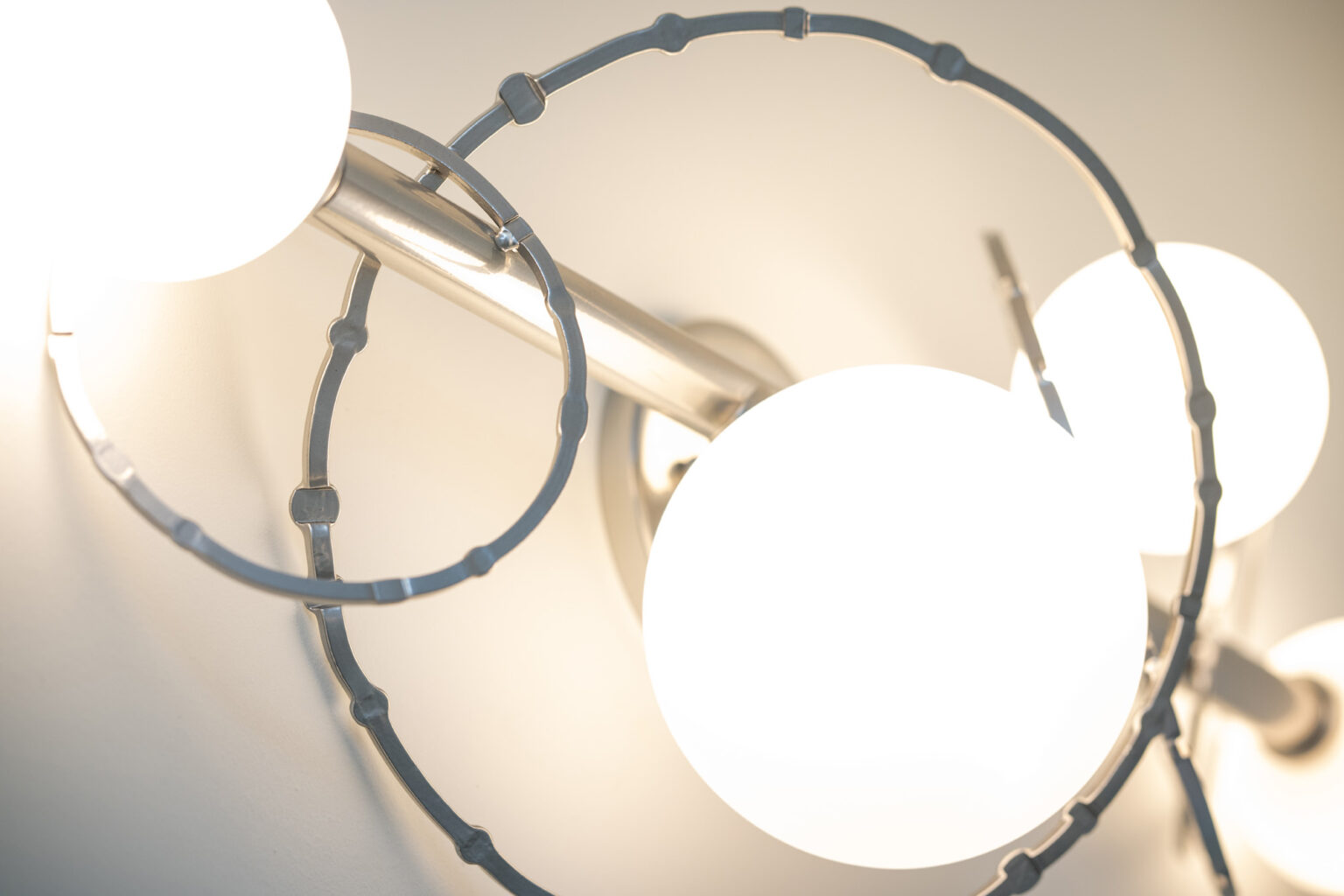 Image by Lesnick Photo Close-up of a modern light fixture with three white spherical bulbs and silver circular metal accents.