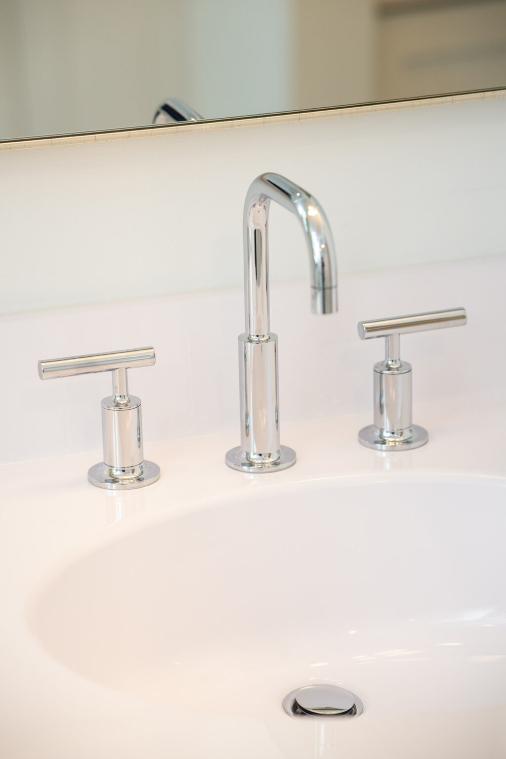 Image by Lesnick Photo A close-up of a modern bathroom sink with a sleek chrome faucet and two matching handles on a white counter.