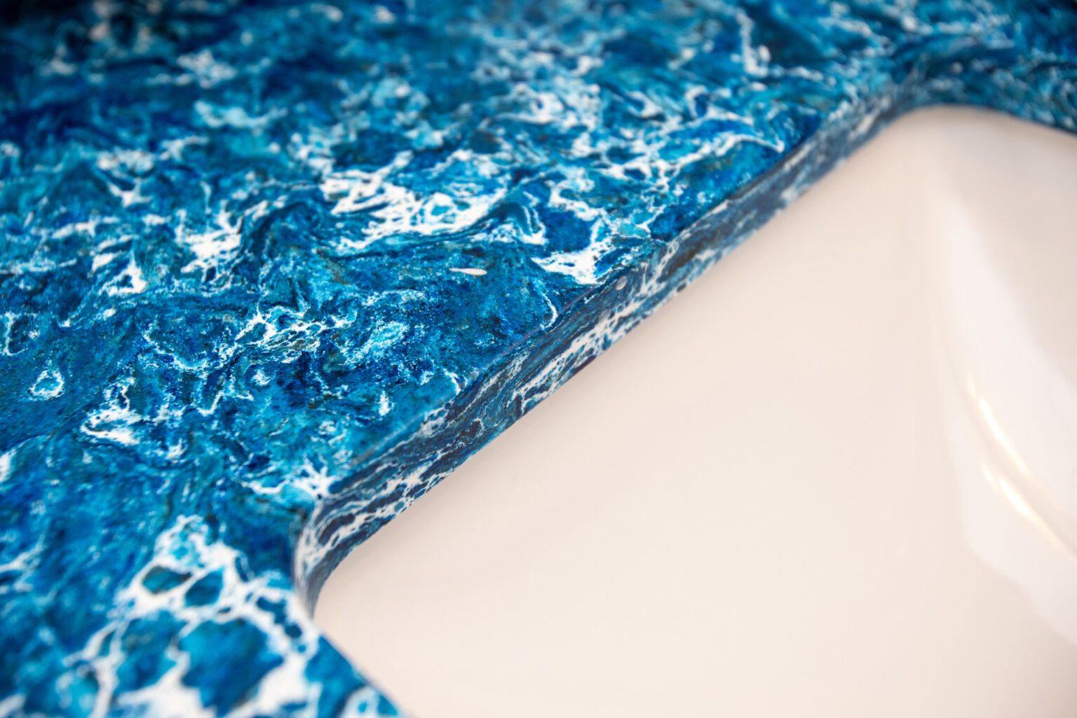 Image by Lesnick Photo Close-up of a bathroom countertop with a blue and white marbled pattern surrounding a beige sink.
