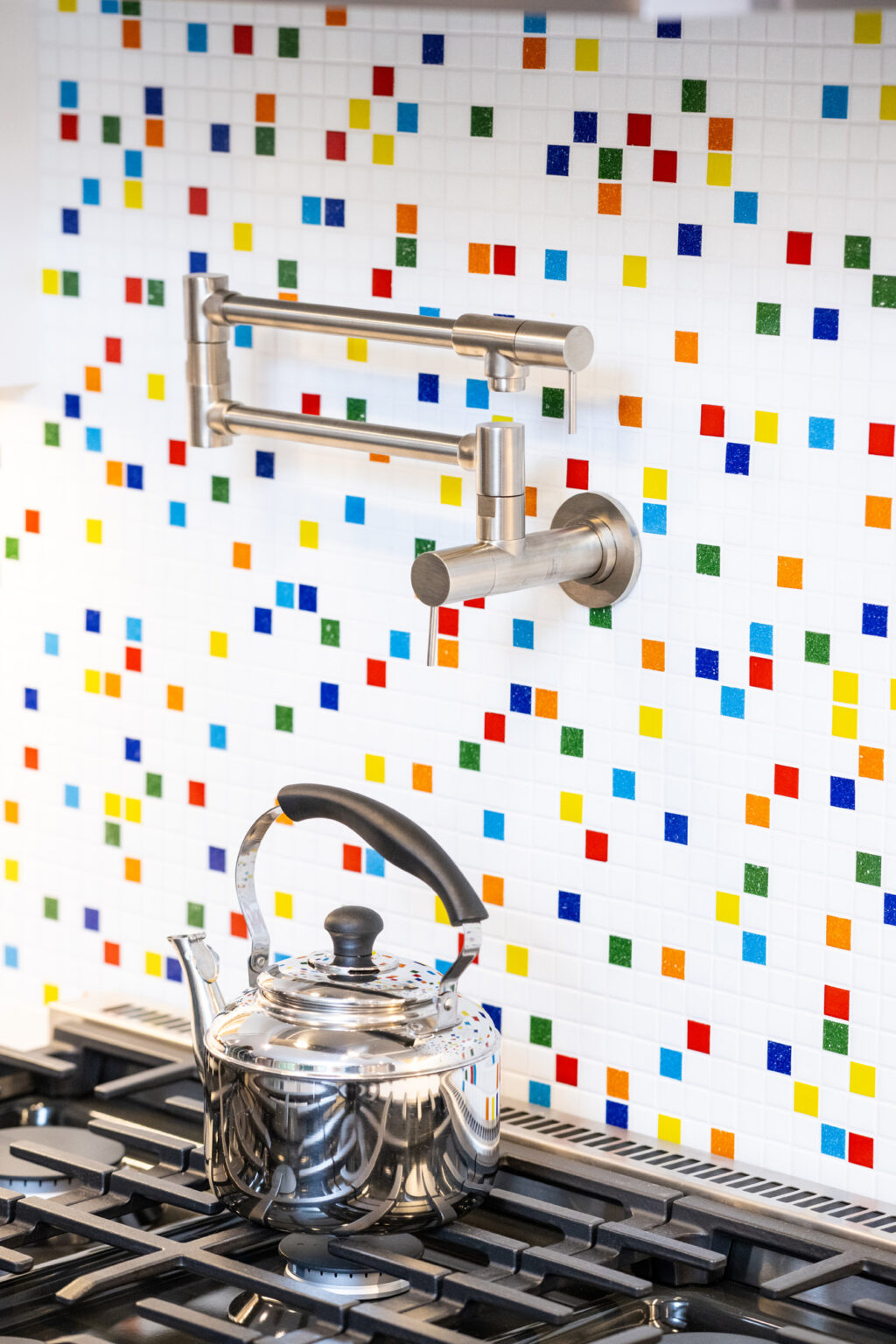 Image by Lesnick Photo Stainless steel kettle on a gas stove with a vibrant mosaic tile backsplash and a wall-mounted pot filler faucet above.