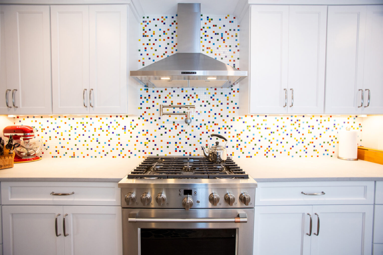 Image by Lesnick Photo Modern kitchen featuring a stainless steel stove with a colorful tile backsplash, white cabinets, and a mixer on the left countertop.
