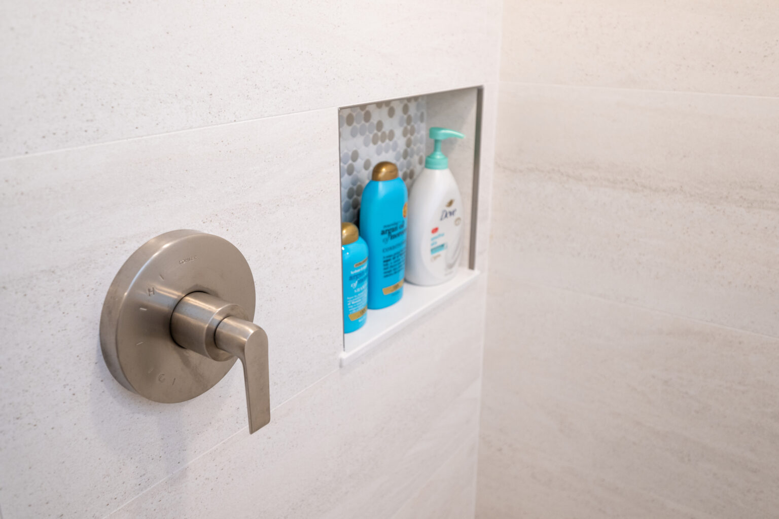 Shower wall with a stainless steel handle and a built-in shelf holding various toiletries.