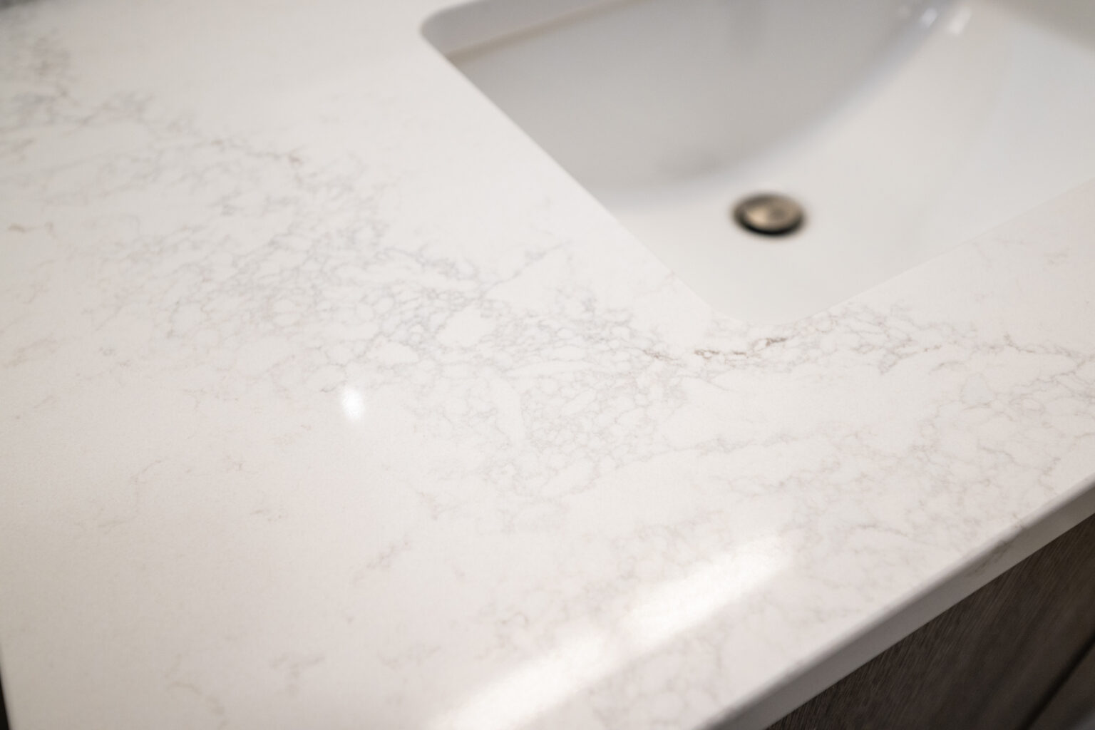 A close-up view of a white marble countertop with subtle grey veining, featuring an integrated sink with a silver drain.