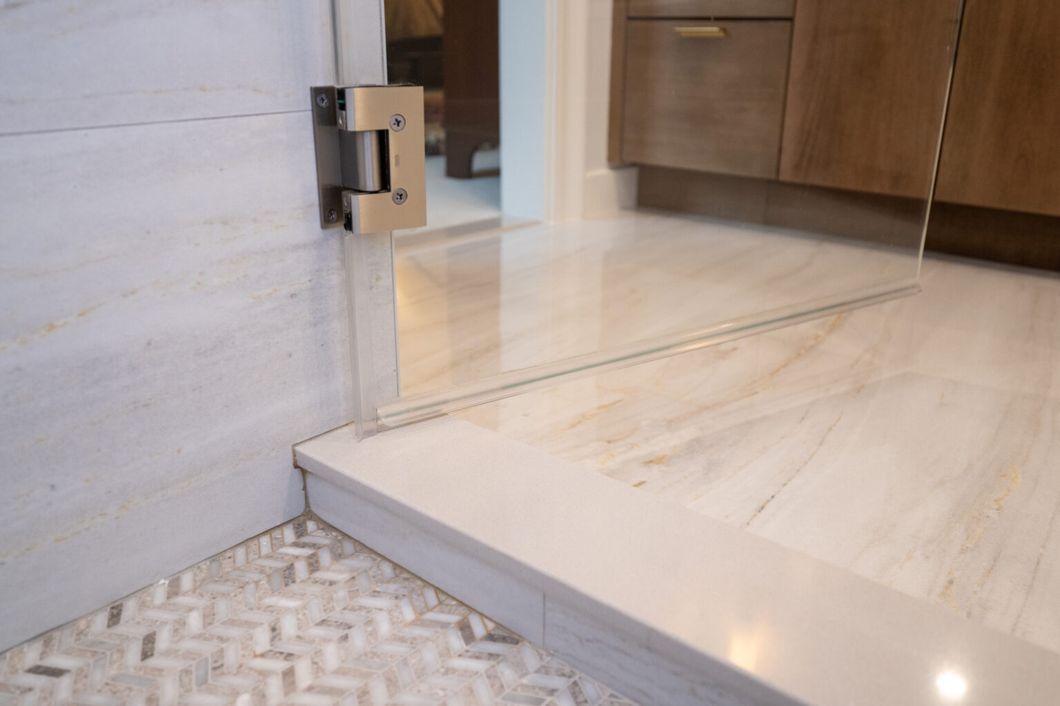 Close-up view of a glass shower door with metallic hinges, adjacent to a tiled bathroom floor.