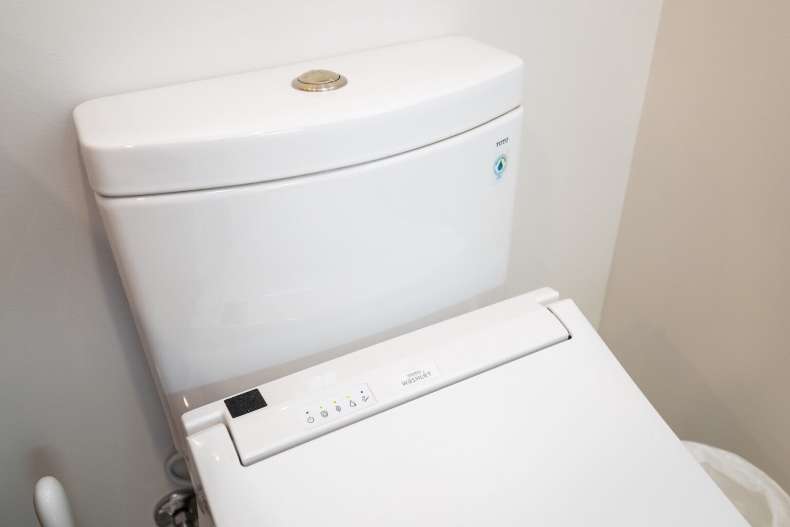 A close-up view of a modern white toilet with a control panel on the seat and a silver flush button on the tank.